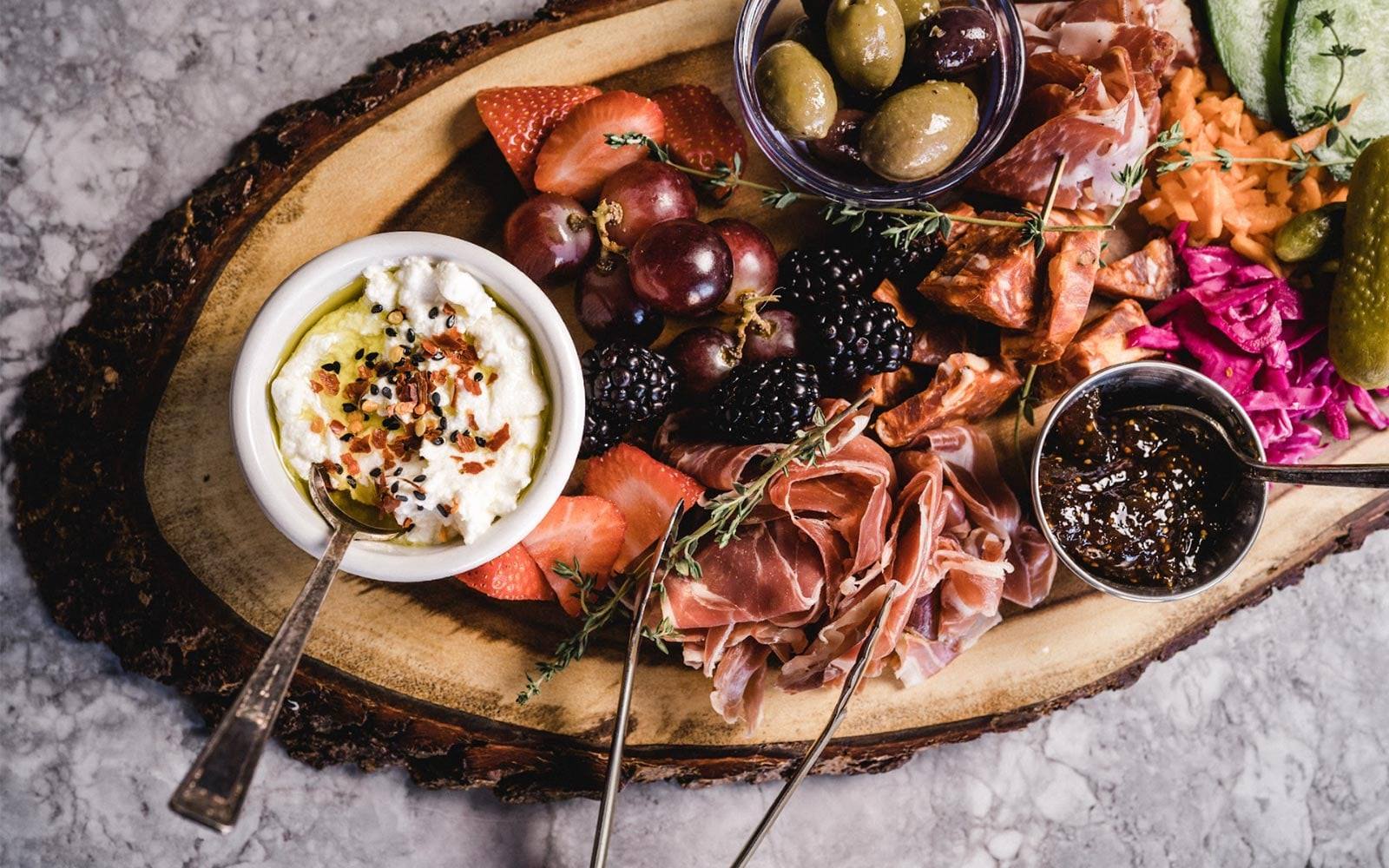 A charcuterie board with cured meats, cheese, olives and fresh fruit